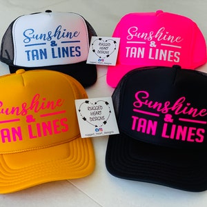 Puede incluir: Cuatro gorras de camionero en negro, blanco, rosa ne&oacute;n y amarillo, cada una con el texto Sunshine & TAN LINES en colores contrastantes. Se ven dos peque&ntilde;as etiquetas cuadradas blancas con el texto RUGGED HEART DESIGNS e iconos sociales.