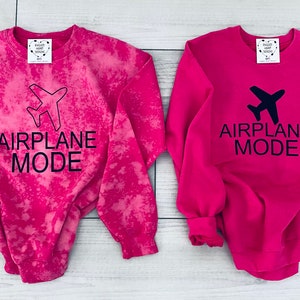 May include: Two pink sweatshirts with the text "AIRPLANE MODE" and a black airplane graphic. One sweatshirt has a tie-dye pattern.