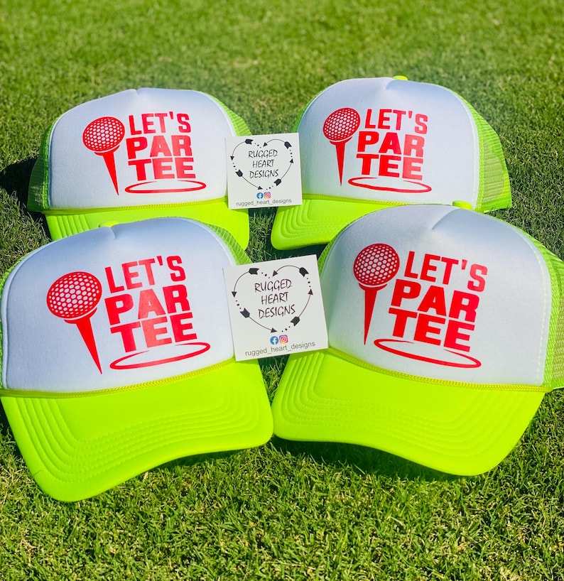 May include: Four golf trucker hats with white fronts and neon green brims and mesh backs. Each hat features the text "LET'S PAR TEE" in red with a golf ball and tee graphic. Small cards with the text "RUGGED HEART DESIGNS" are also present.