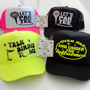 May include: Four trucker hats with golf-themed designs. One is neon pink and white with "LET'S PAR TEE". Another is black with the same text. A neon yellow hat says "TALK BIRDIE TO ME". The last is black with "OVER PAR AND UNDER THE INFLUENCE".