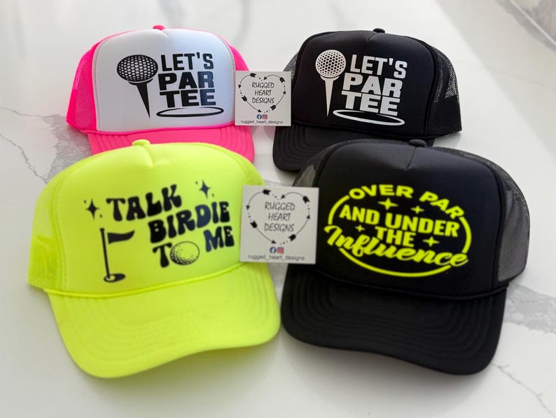 May include: Four trucker hats with golf-themed designs. One is neon pink and white with "LET'S PAR TEE". Another is black with the same text. A neon yellow hat says "TALK BIRDIE TO ME". The last is black with "OVER PAR AND UNDER THE INFLUENCE".