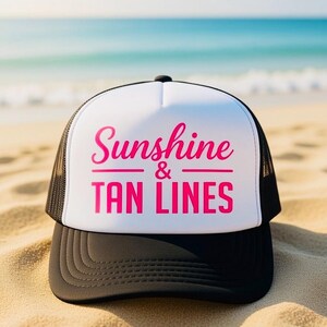 Puede incluir: Una gorra de camionero negra y blanca con un panel frontal blanco que presenta el texto en rosa intenso Sunshine & TAN LINES impreso en una mezcla de fuentes cursivas y de bloque. La gorra incluye una visera negra y paneles de malla negros.