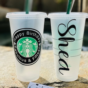 May include: Two clear plastic cups with black text and designs. The first cup says "Happy Birthday Fabulous & Fifteen" with a green Starbucks logo. The second cup says "Shea" in a cursive font. Both cups have a black line for a straw.
