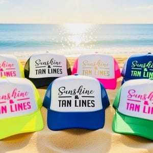 Puede incluir: Una colecci&oacute;n de seis gorras de camionero en varios colores, incluyendo amarillo ne&oacute;n, negro, rosa, azul y verde. Cada gorra presenta un panel frontal blanco con el texto Sunshine & TAN LINES impreso en una mezcla de letra cursiva y de molde.