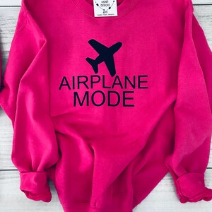 May include: A pink sweatshirt with the text "AIRPLANE MODE" in black lettering and a black airplane graphic above the text.