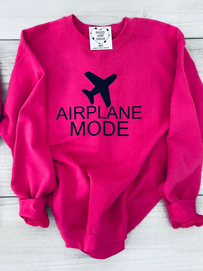 May include: A pink sweatshirt with the text "AIRPLANE MODE" in black lettering and a black airplane graphic above the text.