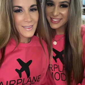 May include: Two women wearing pink sweatshirts with black airplane graphics and the text "Airplane Mode" and "RPLA MOD".