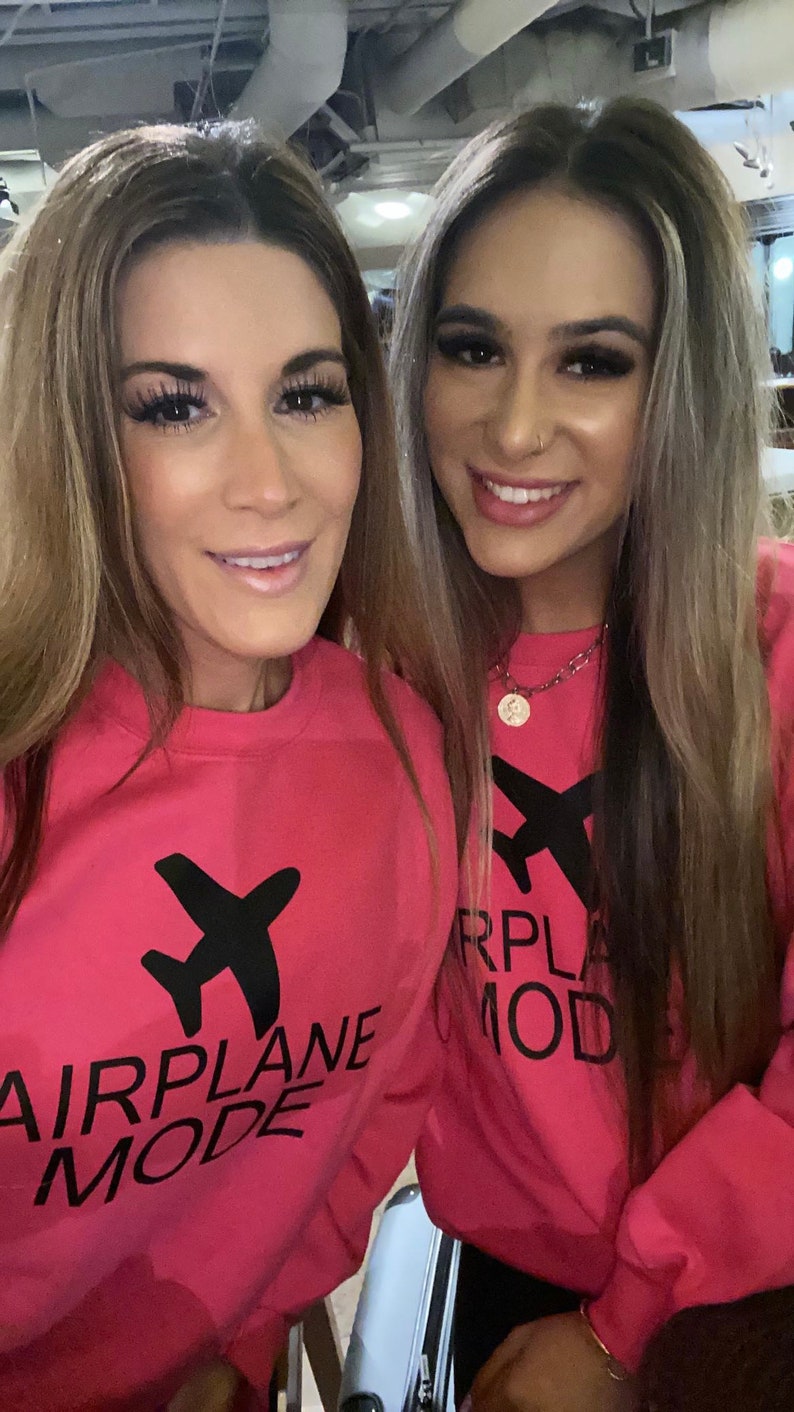 May include: Two women wearing pink sweatshirts with black airplane graphics and the text "Airplane Mode" and "RPLA MOD".