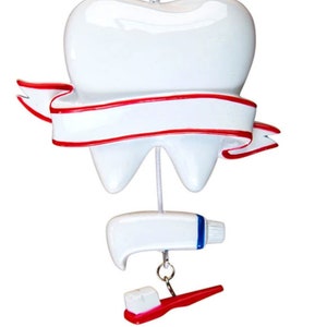 May include: A white tooth ornament with a red ribbon and a white banner. The tooth is hanging from a string with a white tube of toothpaste and a red toothbrush hanging below.
