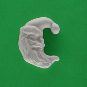 May include: White ceramic ornament shaped like a Santa Claus head with a beard and a hat. The ornament is in the shape of a crescent moon.