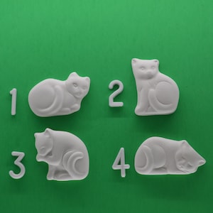 May include: Four white ceramic cat figurines on a green background. Each cat is in a different pose and is numbered 1 through 4.