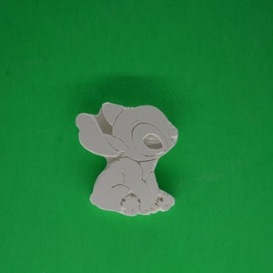 May include: White ceramic figurine of Stitch from the Disney movie Lilo & Stitch. Stitch is sitting with his arms crossed and his head tilted to the side.