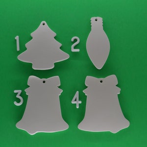 May include: Four blank white ceramic ornaments, numbered 1 through 4. The ornaments are shaped like a Christmas tree, a light bulb, and two bells.