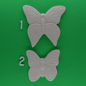 May include: Two white ceramic butterfly shapes on a green background. The butterflies are numbered 1 and 2.
