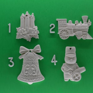 May include: Four white ceramic Christmas ornaments on a green background. The ornaments are numbered 1 through 4. Ornament 1 is a candle holder, ornament 2 is a train, ornament 3 is a bell, and ornament 4 is a soldier with a cannon.