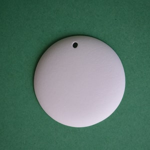 May include: A white round ornament with a hole at the top. The ornament is on a green background.