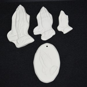 May include: Set of four white ceramic praying hands ornaments. The ornaments are in various sizes and shapes, including a round ornament with a hole for hanging.
