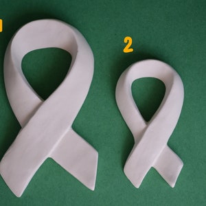 May include: Two white ribbon sculptures on a green background. The ribbon on the left is larger than the ribbon on the right.