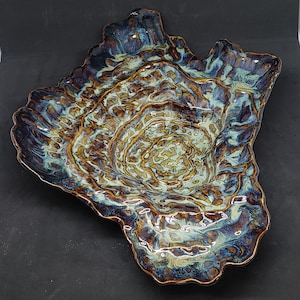 May include: A large, ceramic serving dish with an irregular, organic shape. The dish is glazed in shades of blue, brown, and white, creating a swirling, marbled effect. The centre of the dish is a deep, rounded bowl.