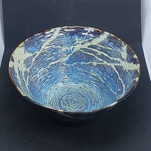 May include: A large, blue and white ceramic bowl with a swirling, textured design. The bowl has a dark brown rim and a glossy finish.