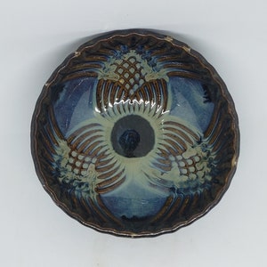 May include: A blue and brown ceramic bowl with a decorative design of pineapples. The bowl has a scalloped edge and a raised centre.