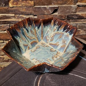 May include: A brown and blue ceramic bowl with a starburst shape and a white glaze. The bowl has a unique design with a swirling pattern.