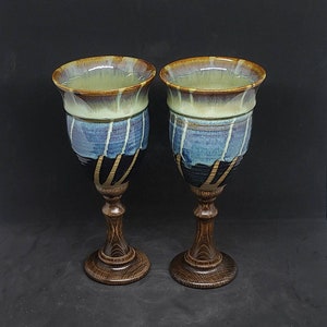 May include: Two ceramic goblets with a blue and brown glaze and wooden stems. The goblets are on a black background.