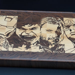 May include: A wooden cutting board with a checkered pattern, featuring laser-etched images of four popular superhero characters: Iron Man, Hulk, Thor, and Captain America.