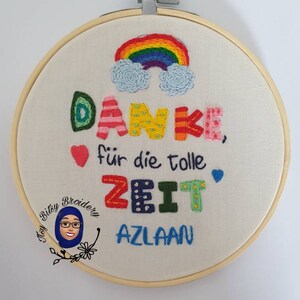 May include: Embroidered hoop art featuring a rainbow and multi-coloured text. The text reads "DANKE, f&uuml;r die tolle ZEIT AZLAAN". The embroidery is set in a wooden hoop. A small logo is in the lower left corner.