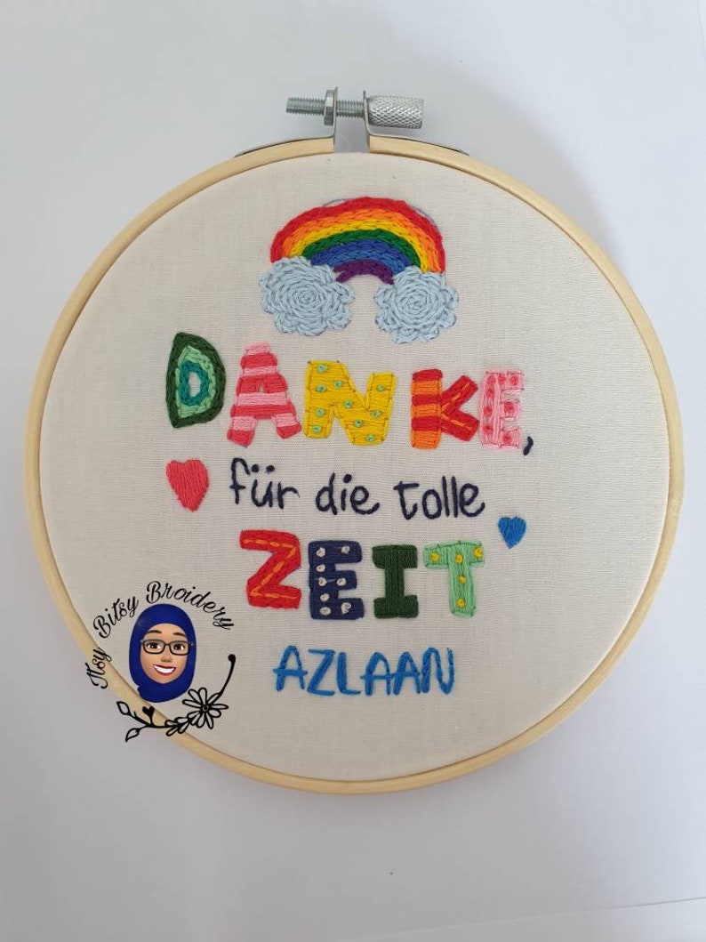 May include: Embroidered hoop art featuring a rainbow and multi-coloured text. The text reads "DANKE, f&uuml;r die tolle ZEIT AZLAAN". The embroidery is set in a wooden hoop. A small logo is in the lower left corner.