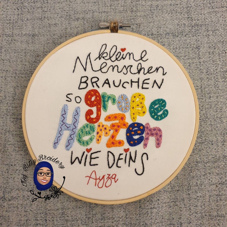 May include: Embroidered hoop art with the German text "kleine Menschen brauchen so gro&szlig;e Herzen wie deins" in various colours. The hoop is made of wood and the text is stitched on white fabric. The name "Ayza" is stitched in red.