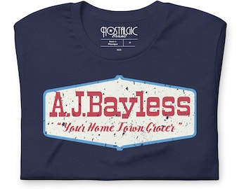May include: Navy blue t-shirt with a distressed graphic. The graphic features the text "A.J.Bayless" in red, with "Your Home Town Grocer" below it. The shirt has a crew neck and is made of 100% cotton.