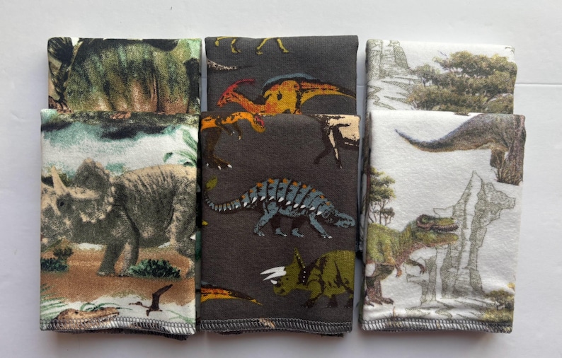 May include: Six fabric squares with different dinosaur patterns. The squares are brown, white, and green with various dinosaur illustrations.