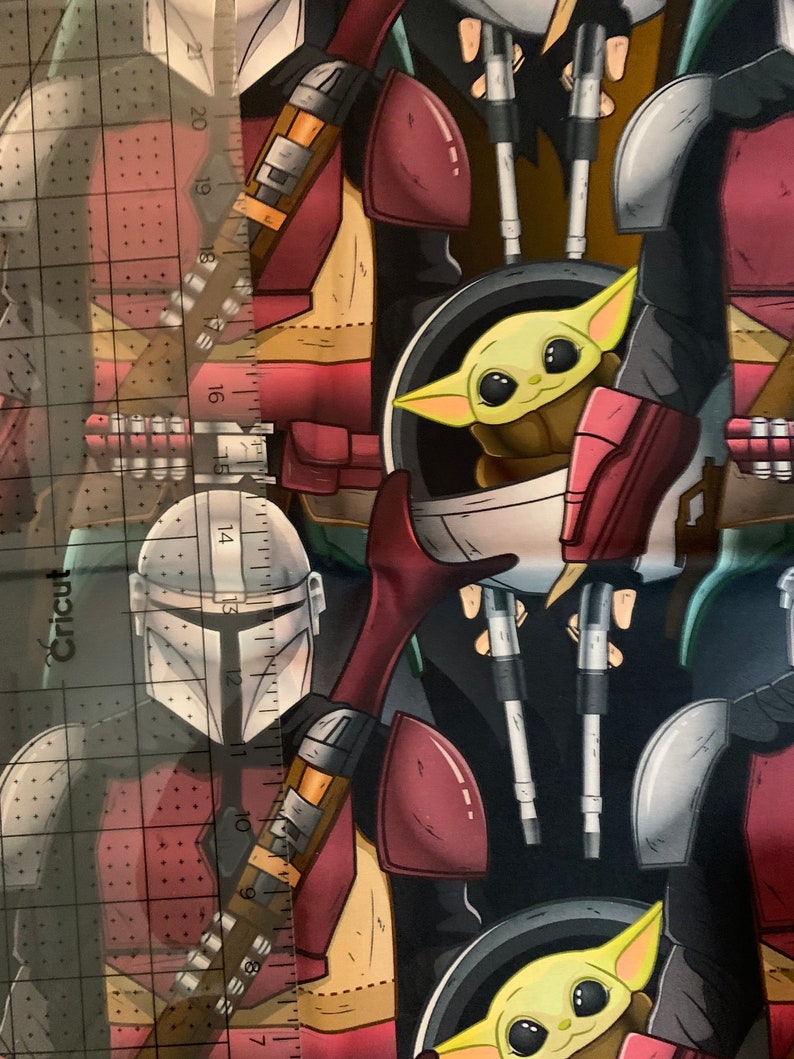 Może przedstawiać: Czarno-zielony materiał z powtarzającym się wzorem postaci Mandalorianina i postaci Baby Yody. Mandalorianin ma na sobie hełm i trzyma broń. Baby Yoda ma na sobie brązową szatę i siedzi w kapsule.