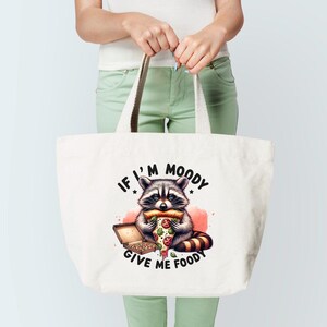 May include: White canvas tote bag with a cartoon raccoon eating a pizza slice. The text on the bag reads "If I'm Moody Give Me Foody".