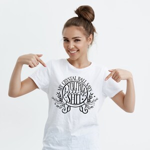 May include: White t-shirt with a black graphic design that says "My Crystal Ball Says You're Full of Shit" with a circle around the text and a floral design.