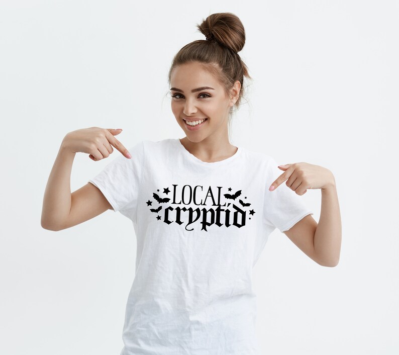 May include: White t-shirt with black text that reads "LOCAL cryptid" with bats and stars around the text.