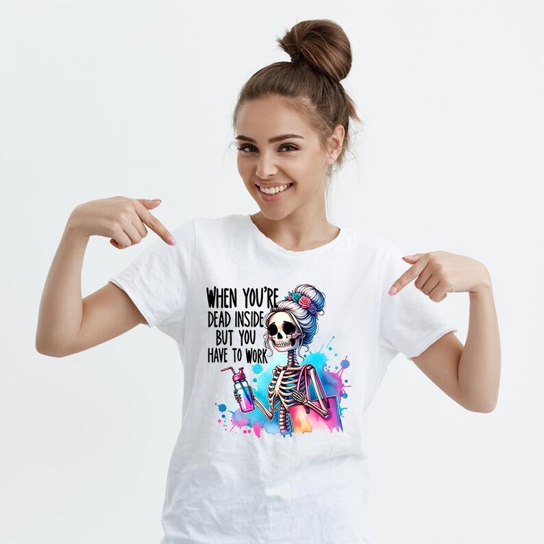 May include: White t-shirt with a colorful graphic of a skeleton with a bun in her hair holding a water bottle and a shopping bag. The text on the shirt reads "When you're dead inside but you have to work."
