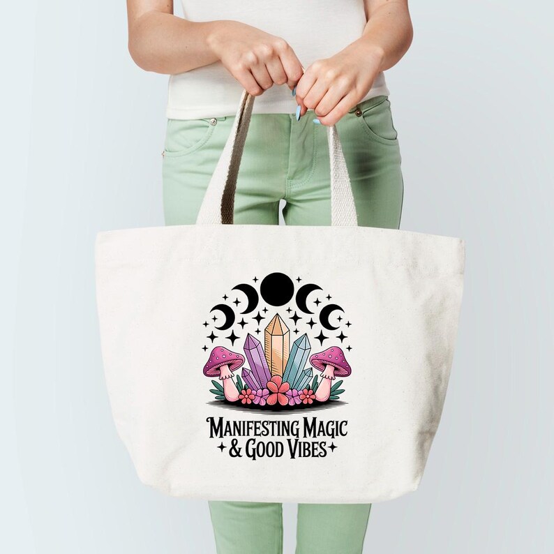 Może przedstawiać: Biała torba typu tote z czarno-białą ilustracją kryształ&oacute;w, grzyb&oacute;w i księżyc&oacute;w. Na torbie nadrukowany jest tekst "MANIFESTING MAGIC + GOOD VIBES +".