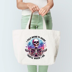 K&ouml;nnte beinhalten: Wei&szlig;e Tragetasche mit farbenfroher Skelettgrafik und dem Text "I fully intend to haunt people when I die." Das Skelett ist mit Sch&auml;del und Brustkorb vor einem Hintergrund im Aquarellstil dargestellt. Die Tasche hat beige Griffe.