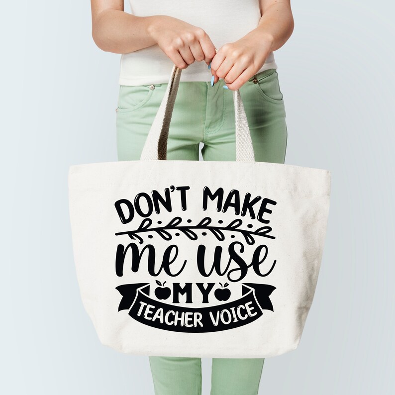 Puede incluir: Una bolsa de lona blanca con texto negro que dice "Don't make me use my teacher voice" con una manzana negra y un dise&ntilde;o de vid negra.