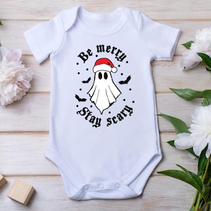 May include: White baby onesie with a black and white graphic of a ghost wearing a Santa hat. The text reads "Be merry. Stay scary."
