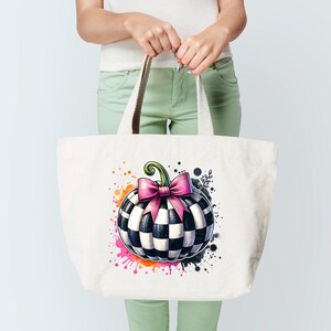May include: A white canvas tote bag featuring a whimsical pumpkin design. The pumpkin is black and white checkered with a pink bow and green stem. Colorful paint splatters surround the pumpkin, adding a playful touch to the design.