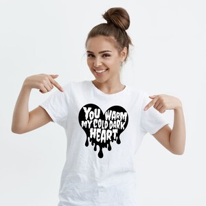 May include: White t-shirt with a black heart graphic that says "You warm my cold dark heart".