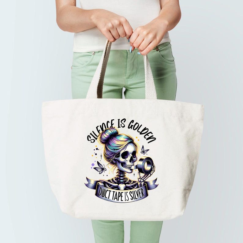 Puede incluir: Una bolsa de tela blanca con una ilustraci&oacute;n colorida de un esqueleto con un mo&ntilde;o en el pelo sosteniendo un rollo de cinta adhesiva. El texto "Silence is Golden Duct Tape is Silver" est&aacute; impreso en la bolsa.