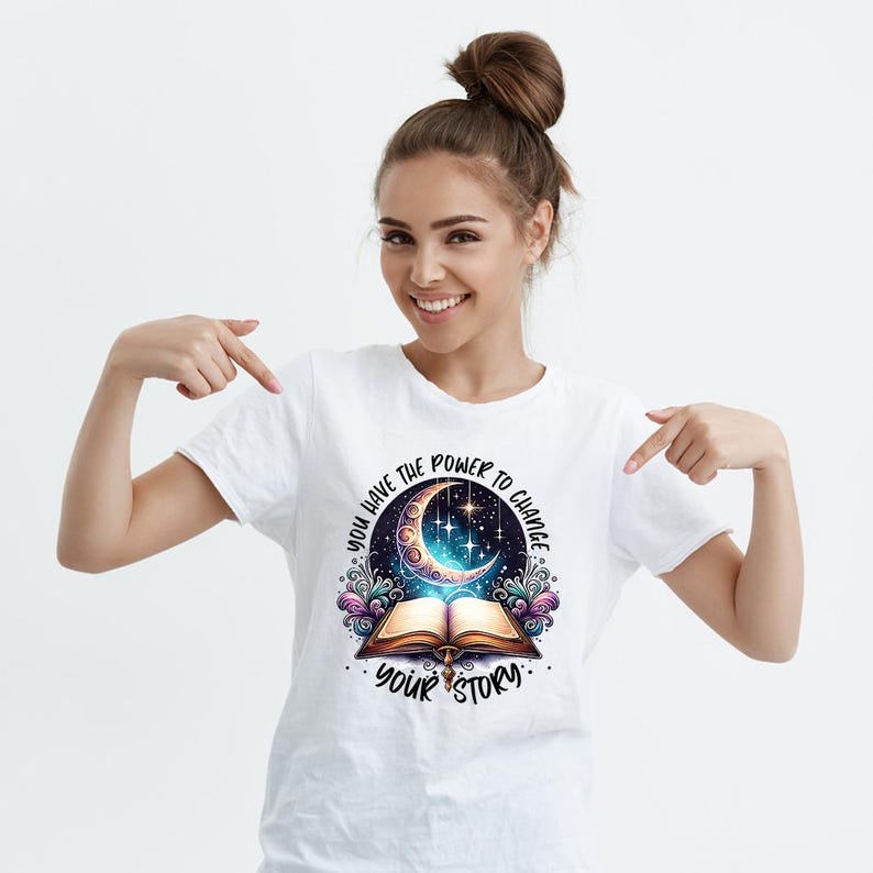 May include: White t-shirt featuring a colorful graphic design. The design includes an open book, a crescent moon, stars, and the text "YOU HAVE THE POWER TO CHANGE YOUR STORY."