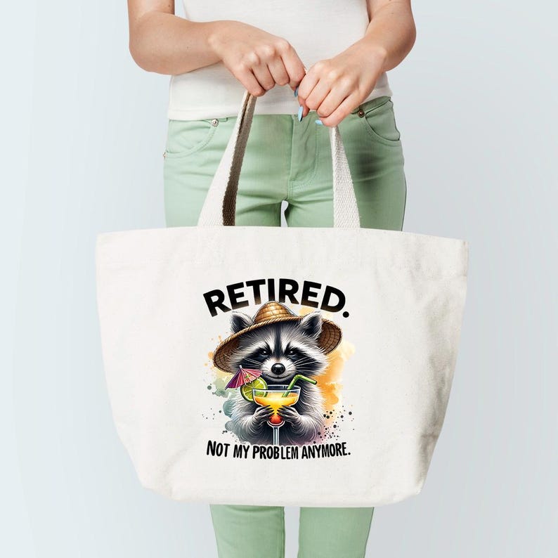 K&ouml;nnte beinhalten: Wei&szlig;e Tragetasche mit einer Grafik eines Waschb&auml;ren mit Strohhut und Cocktail. Der Text "RETIRED. NOT MY PROBLEM ANYMORE." ist &uuml;ber und unter der Waschb&auml;r-Illustration gedruckt. Die Tasche hat cremefarbene Griffe.