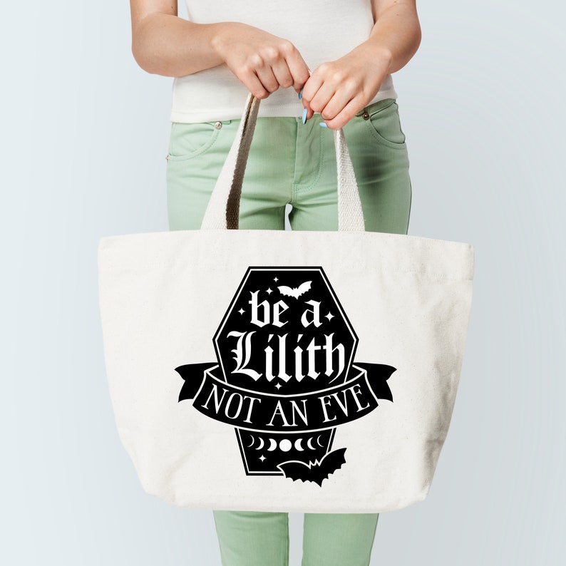 May include: A white tote bag with black text that reads "be a Lilith not an Eve" inside a black coffin shape with a bat and moon phases.