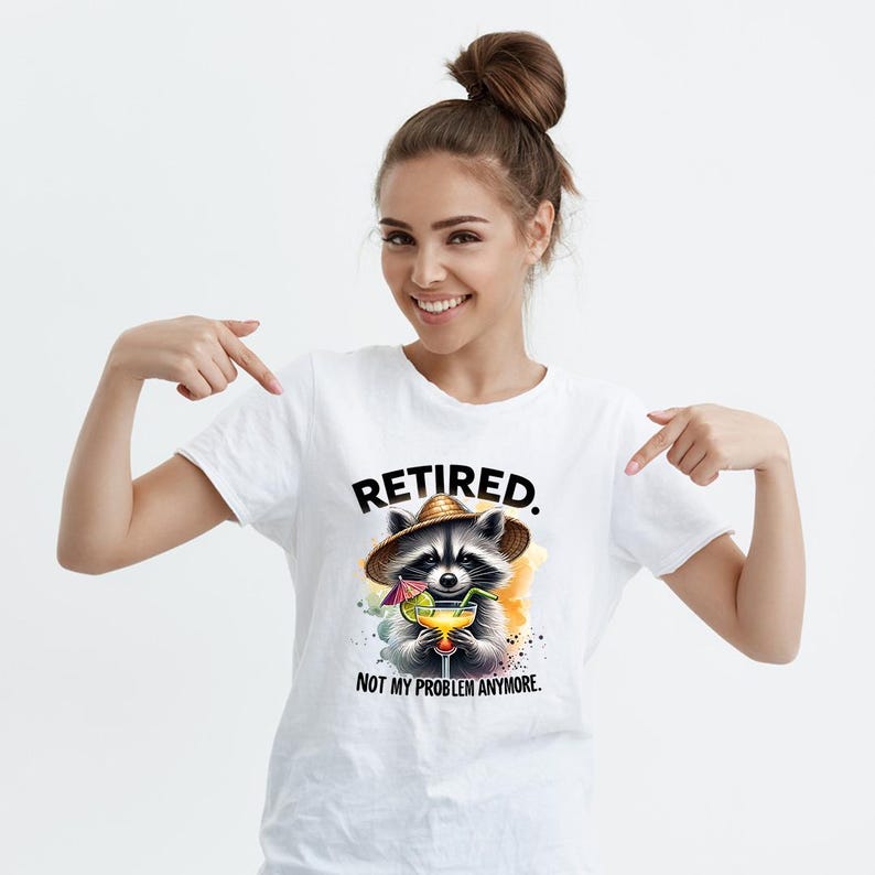 K&ouml;nnte beinhalten: Wei&szlig;es T-Shirt mit einer Illustration eines Waschb&auml;ren, der einen Strohhut tr&auml;gt und einen Cocktail h&auml;lt. Das Design verwendet Aquarelleffekte. Der Text "RETIRED. NOT MY PROBLEM ANYMORE." steht &uuml;ber und unter dem Waschb&auml;ren.