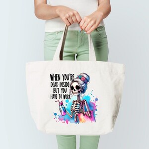 May include: White tote bag with a colorful graphic of a skeleton with a bun and flowers in her hair. The skeleton is holding a water bottle and a purse. The text on the bag reads "When you're dead inside but you have to work."